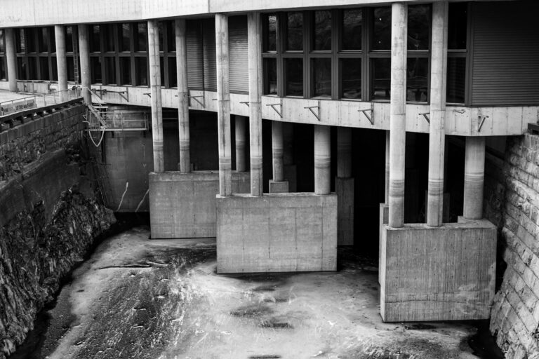 Black and white image of a concrete dam structure with strong industrial elements and architectural details.
