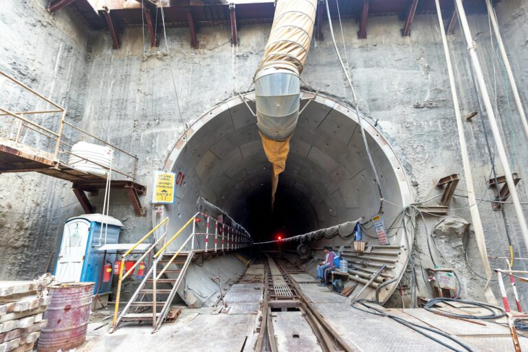 Industrial tunnel entrance under construction with heavy machinery and safety equipment.